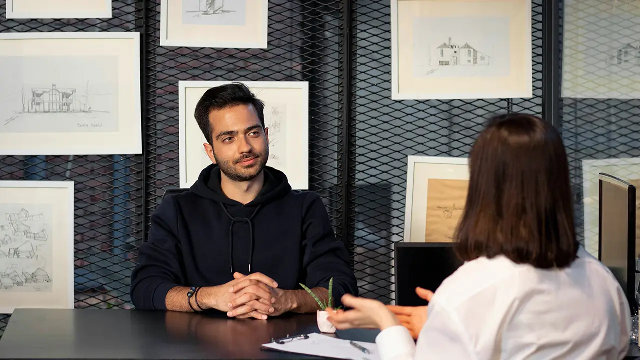 An image of someone interviewing another person across from them at a table.